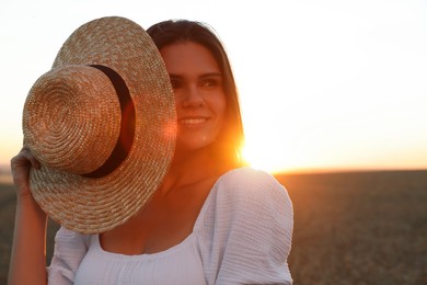 Photo of Beautiful young woman with straw hat in ripe wheat field at sunset, space for text