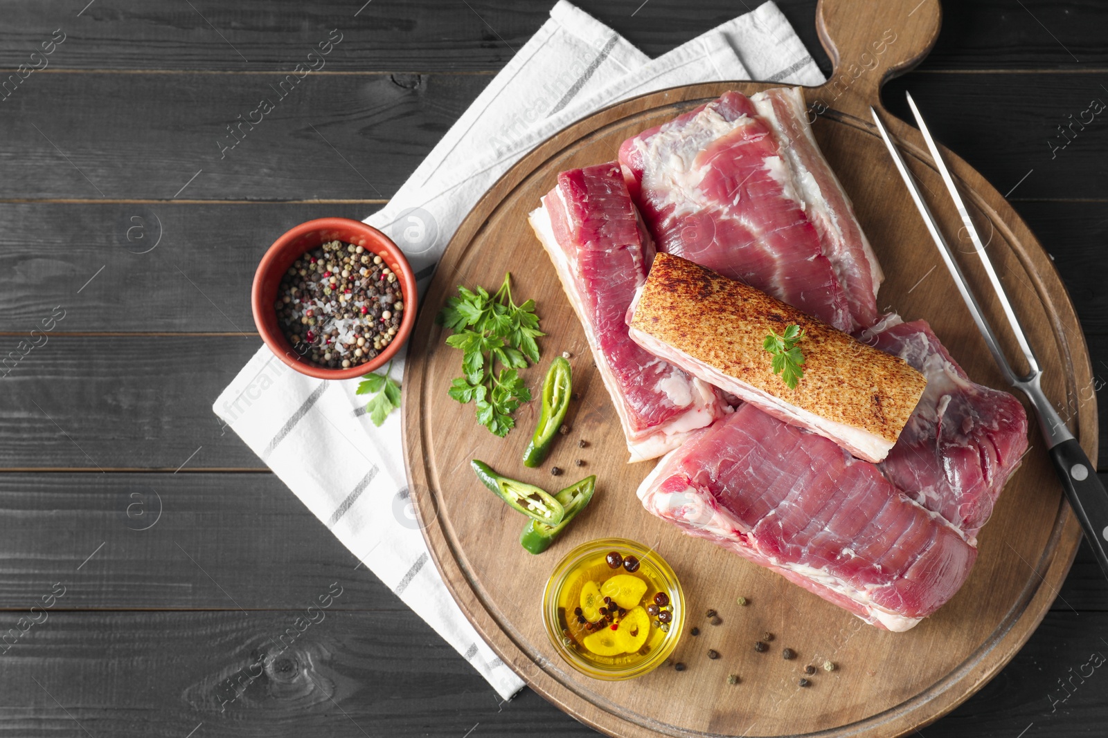 Photo of Pieces of raw pork belly, chili pepper, peppercorns, oil and parsley on black wooden table, top view