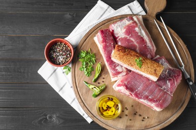 Pieces of raw pork belly, chili pepper, peppercorns, oil and parsley on black wooden table, top view