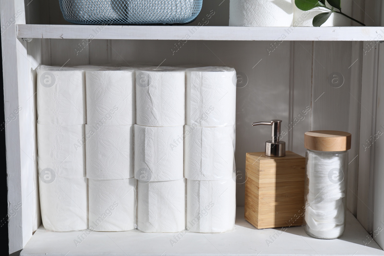 Photo of Toilet paper rolls, dispenser and cotton pads on white shelf