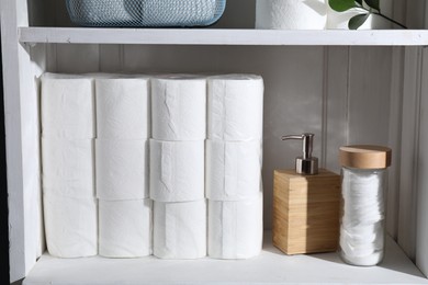 Photo of Toilet paper rolls, dispenser and cotton pads on white shelf