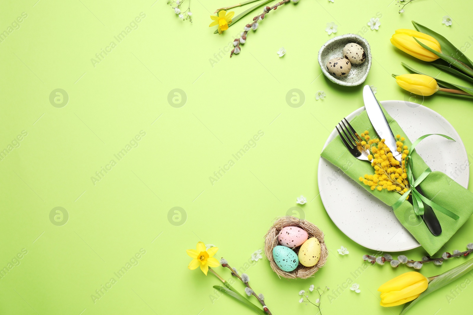 Photo of Festive Easter table setting with eggs and floral decor on green background, flat lay. Space for text