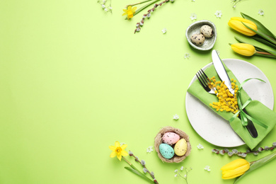 Photo of Festive Easter table setting with eggs and floral decor on green background, flat lay. Space for text