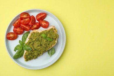 Delicious chicken breast with pesto sauce, tomatoes and basil on yellow table, top view. Space for text