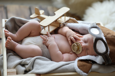 Photo of Cute newborn baby wearing aviator hat with toy sleeping in wooden crate
