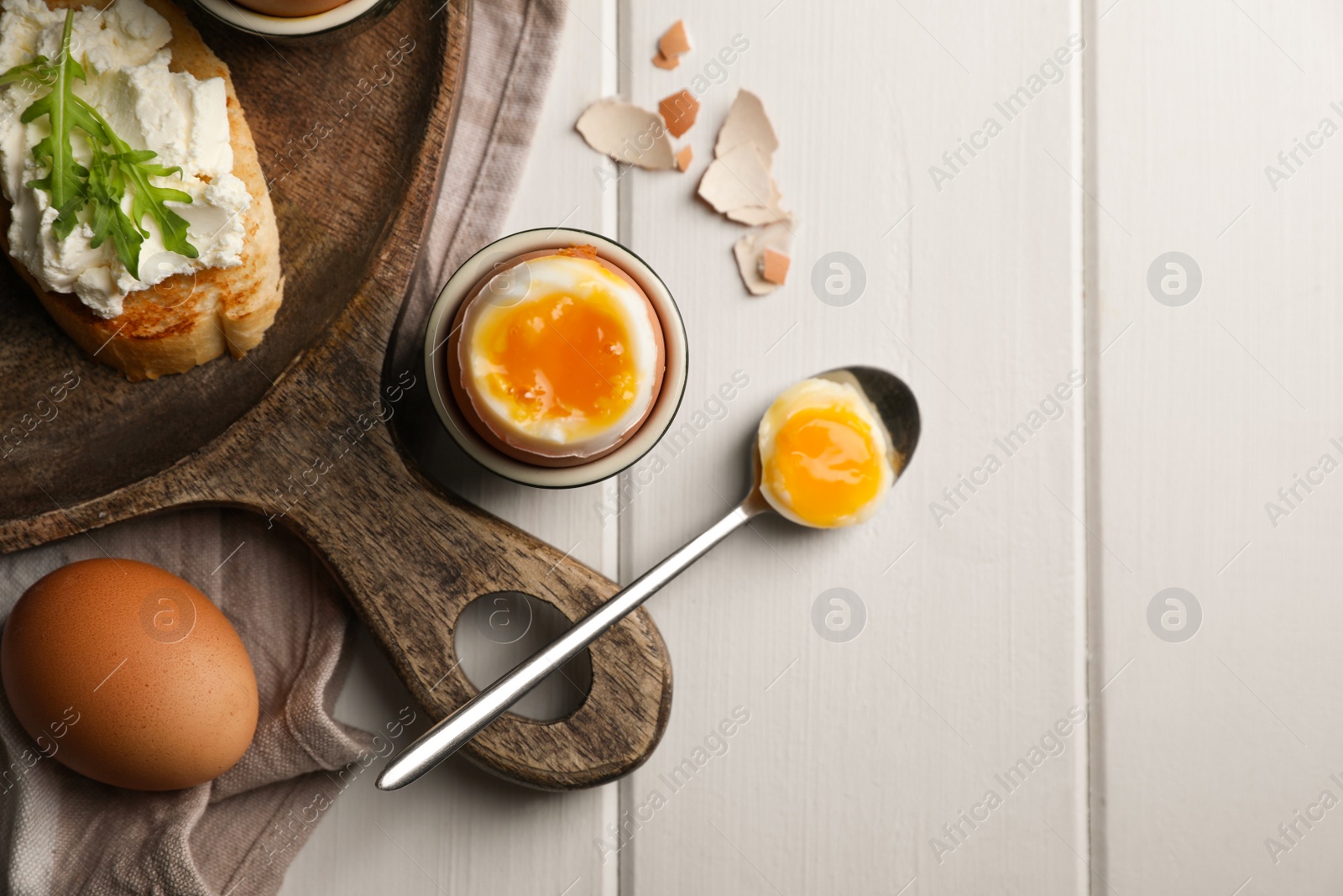 Photo of Breakfast with soft boiled egg served on white wooden table, flat lay. Space for text