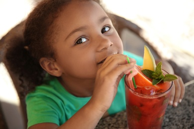 Cute African-American girl with glass of natural lemonade at table in cafe