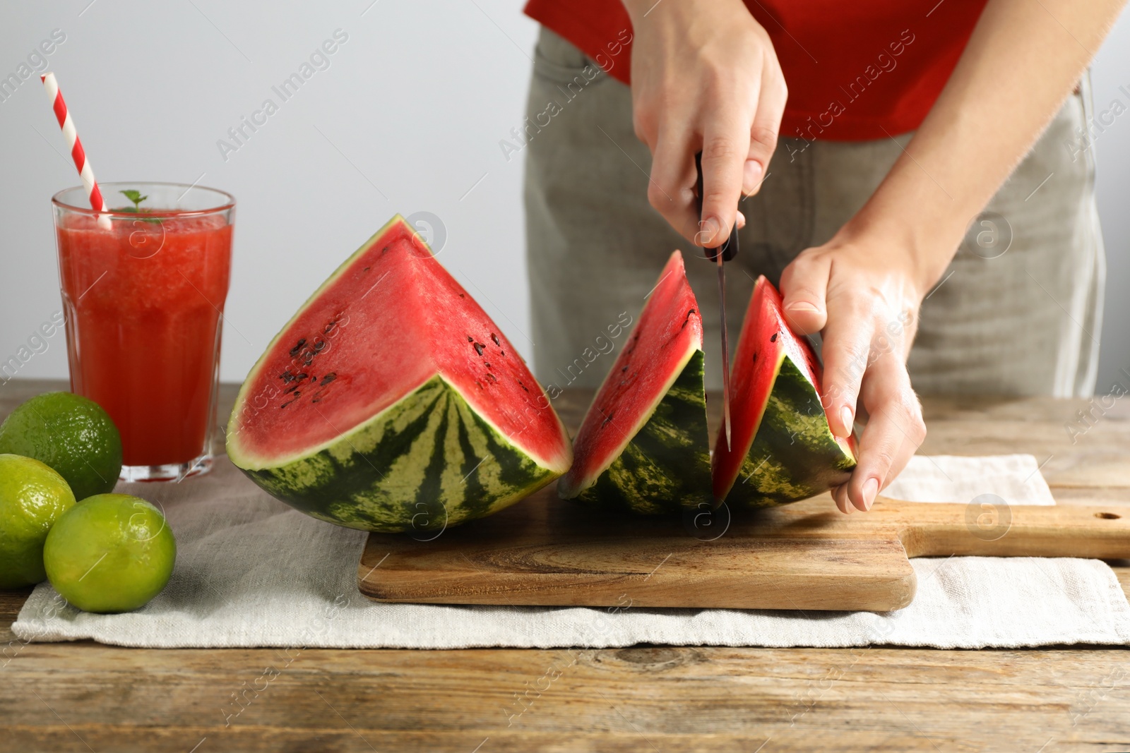 Photo of Woman cutting delicious watermelon at wooden table against light background, closeup