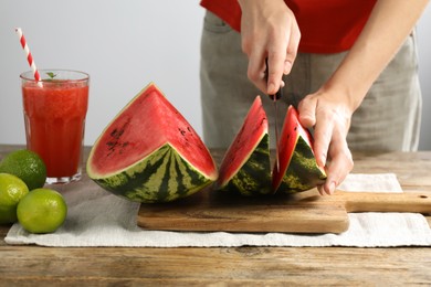 Woman cutting delicious watermelon at wooden table against light background, closeup