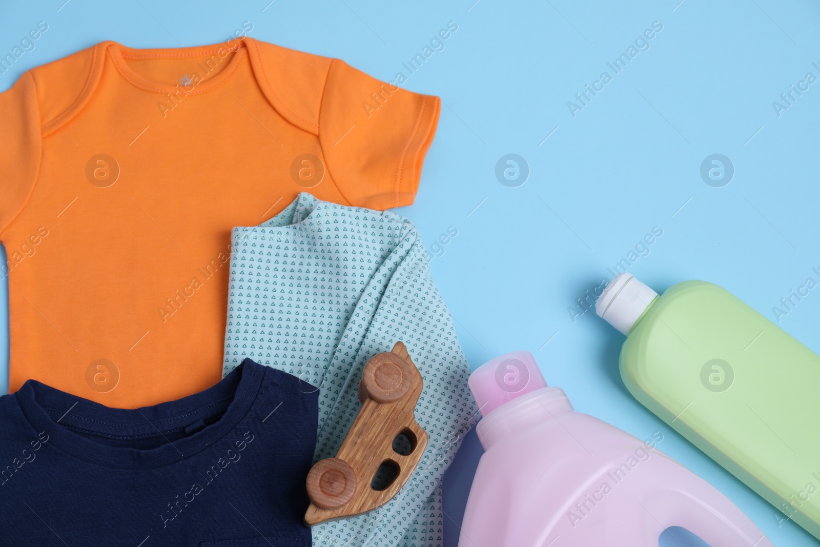 Photo of Bottles of laundry detergents, baby clothes and toy car on light blue background, flat lay. Space for text