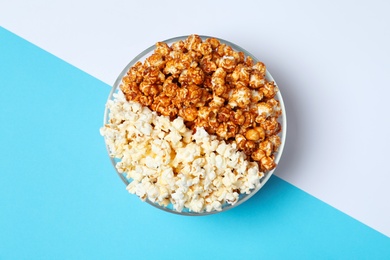 Photo of Different kinds of popcorn in bowl on color background, top view