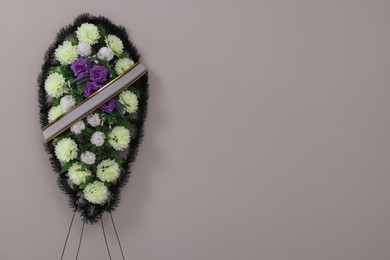 Photo of Funeral wreath of plastic flowers with ribbon on grey background. Space for text
