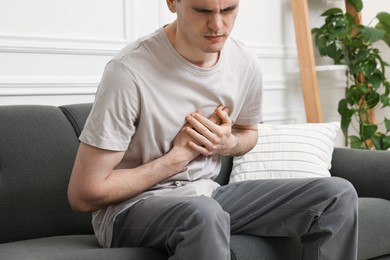 Photo of Young man suffering from heart hurt on sofa at home