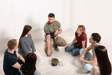 Photo of Soldier in military uniform teaching group of people how to apply medical tourniquet indoors
