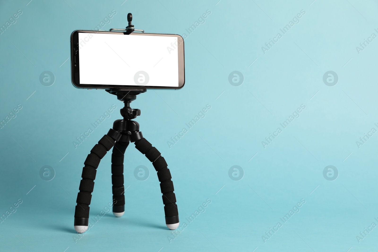 Photo of Modern tripod with smartphone on turquoise background. Space for text