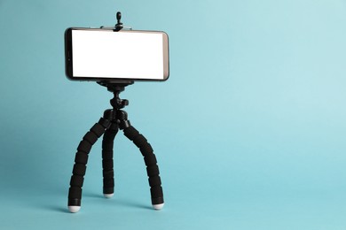 Modern tripod with smartphone on turquoise background. Space for text