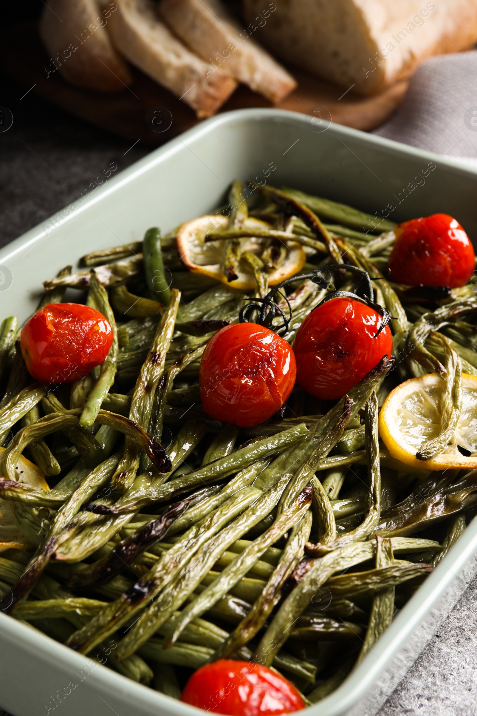 Photo of Delicious baked green beans with lemon and tomatoes in dishware, closeup