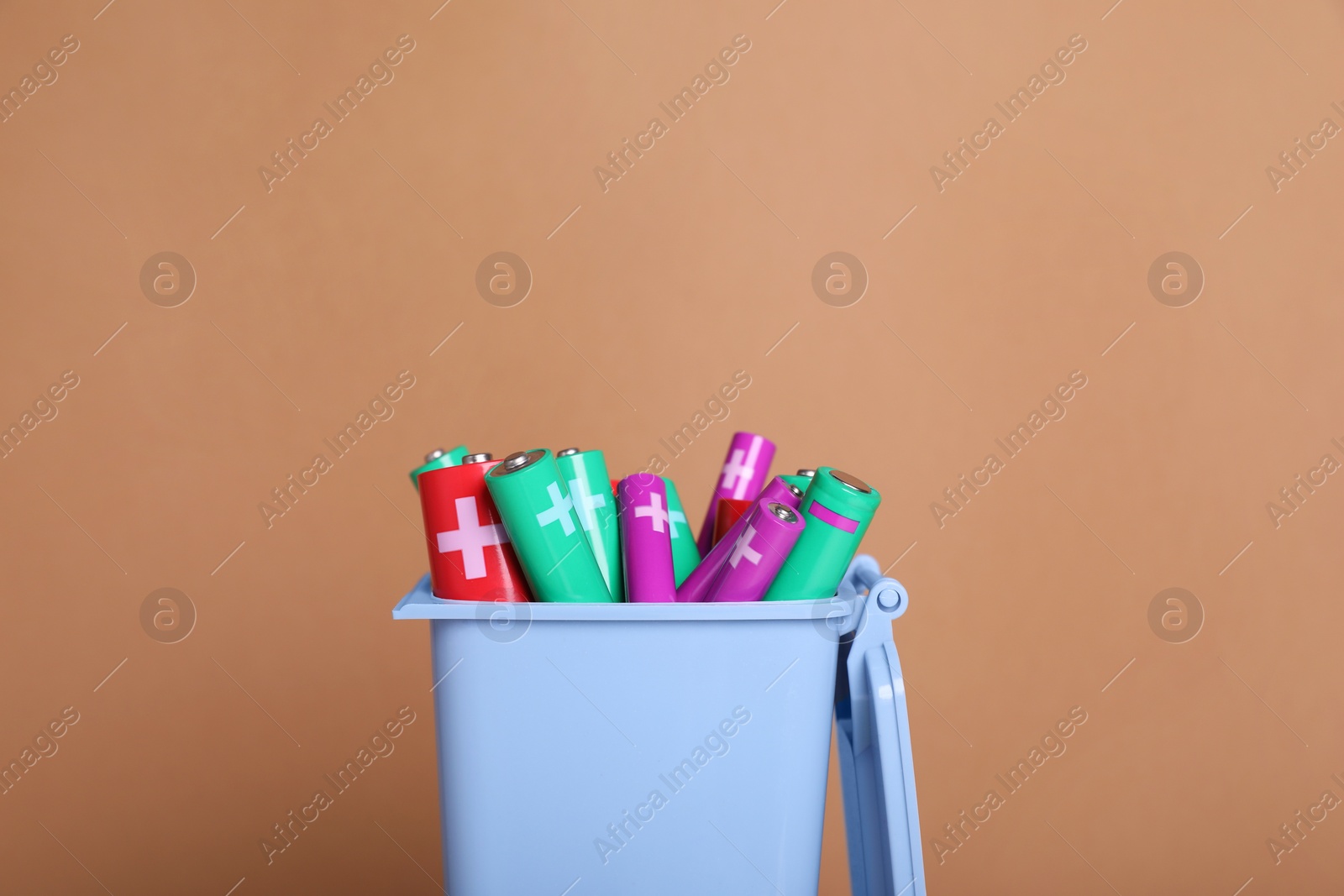 Photo of Many used batteries in recycling bin on light brown background