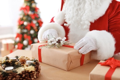 Photo of Authentic Santa Claus wrapping gift at table indoors