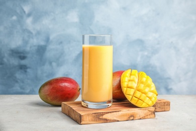 Glass of fresh mango drink and fruits on table against color background