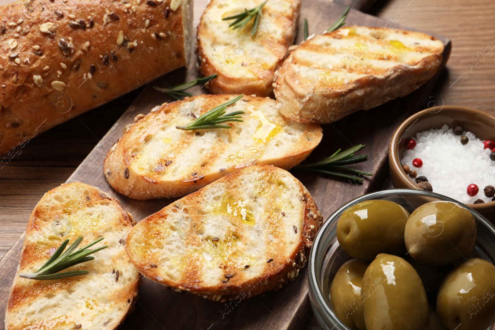 Photo of Tasty bruschettas with oil and rosemary on wooden board, closeup