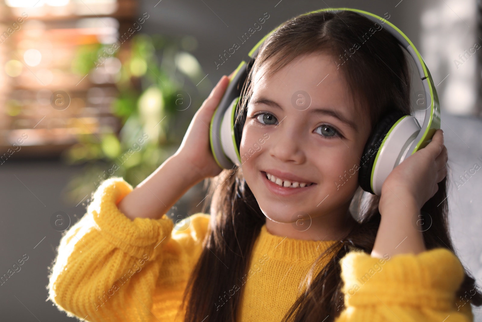 Photo of Cute little girl with headphones listening to audiobook at home