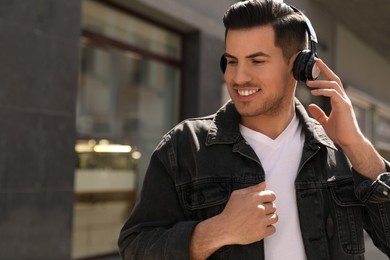 Handsome man with headphones listening to music on city street, space for text