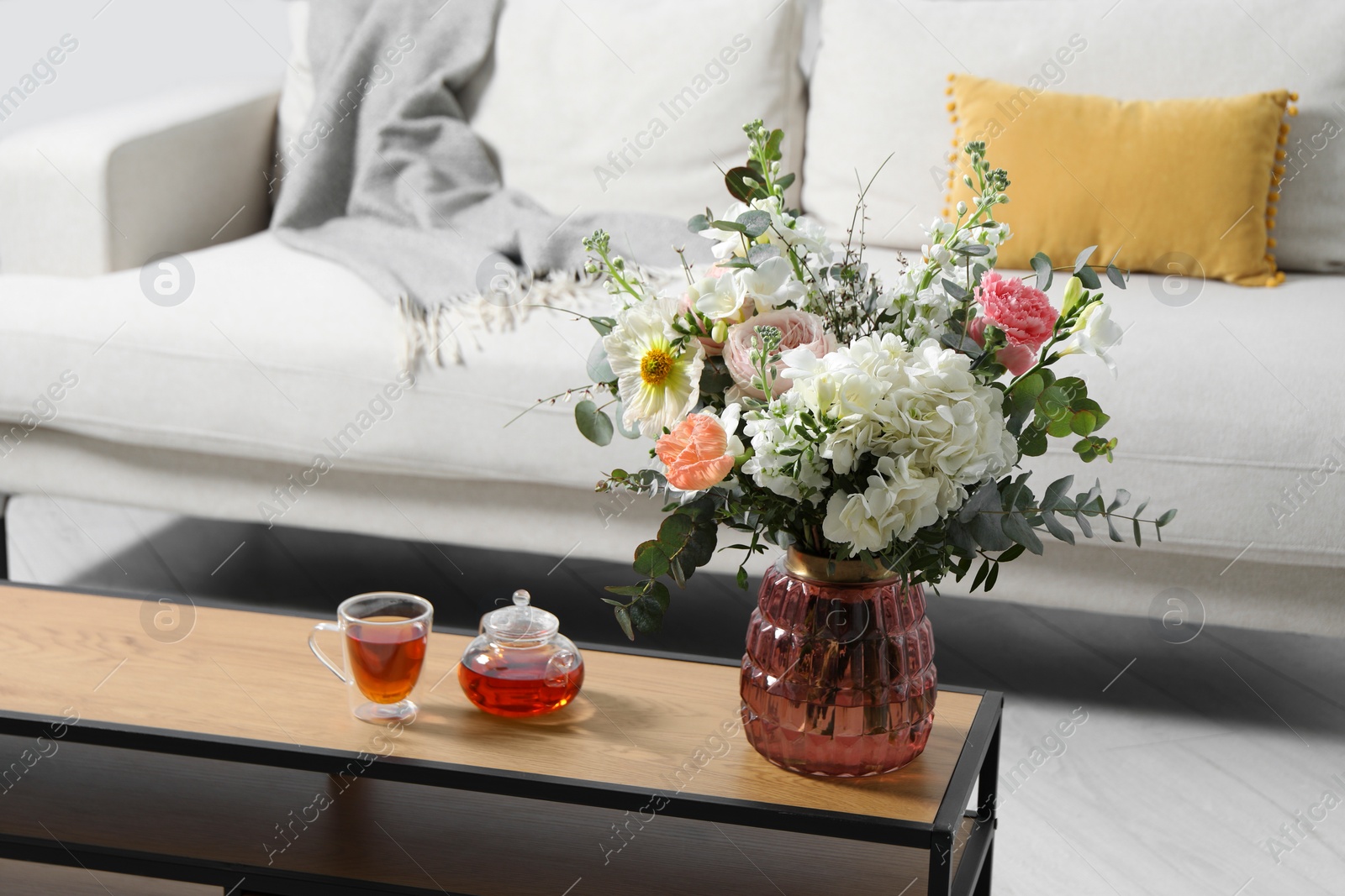 Photo of Bouquet of beautiful flowers and tea on wooden table indoors