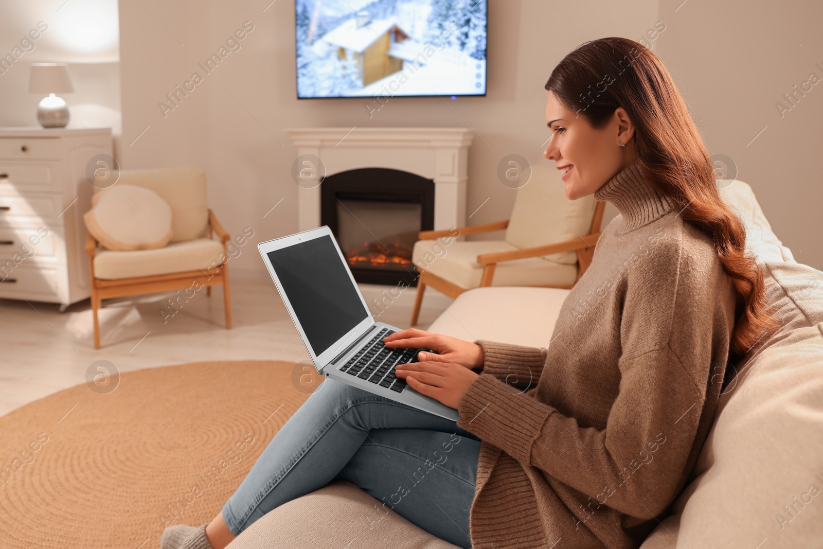 Photo of Young woman with laptop on sofa near fireplace at home