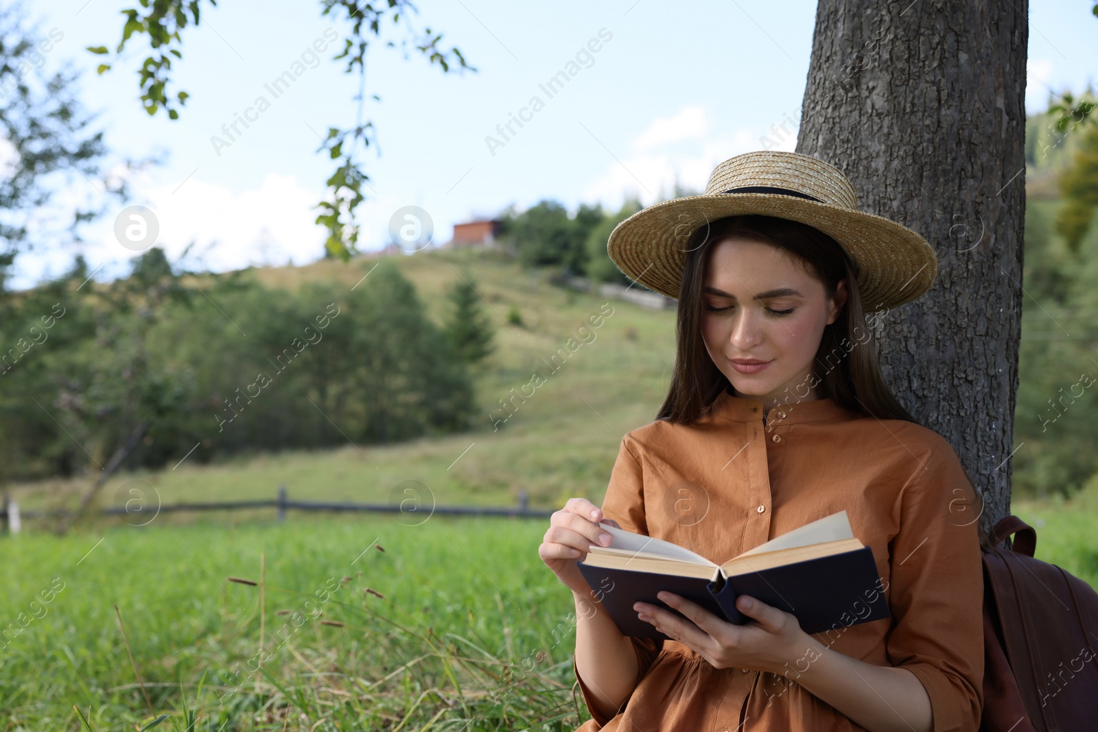 Photo of Young woman reading book under tree on meadow