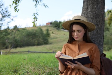 Photo of Young woman reading book under tree on meadow