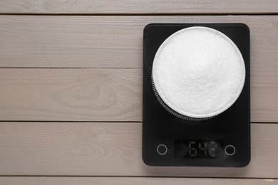 Photo of Electronic scales with sugar on light wooden table, top view. Space for text
