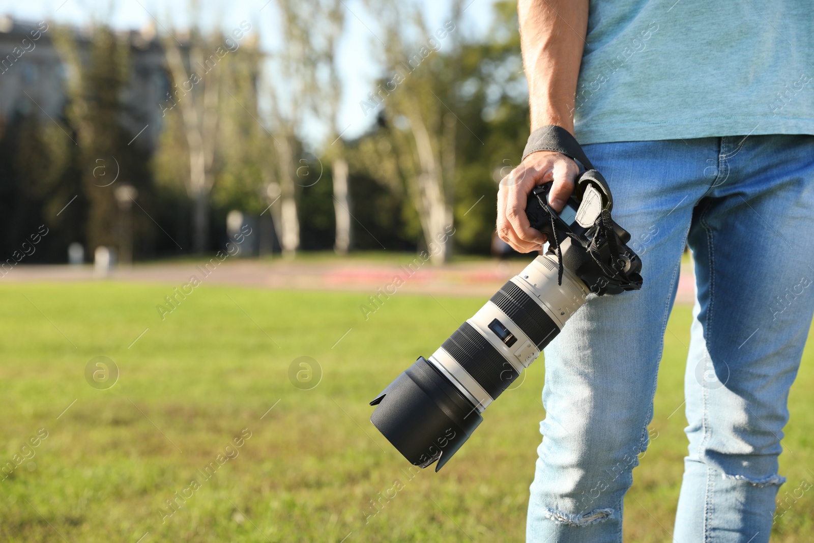 Photo of Young male photographer holding professional camera outdoors. Space for text