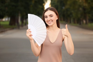 Happy woman holding hand fan in park