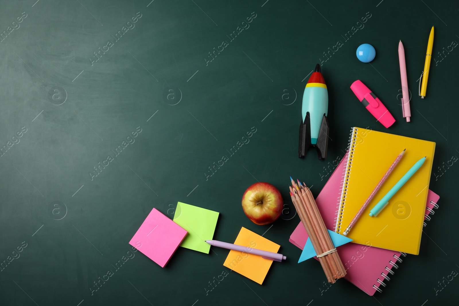 Photo of Bright toy rocket and school supplies on chalkboard, flat lay. Space for text