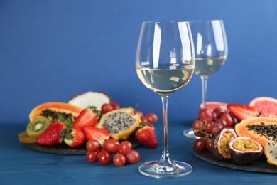 Photo of Delicious exotic fruits and glasses of wine on blue wooden table