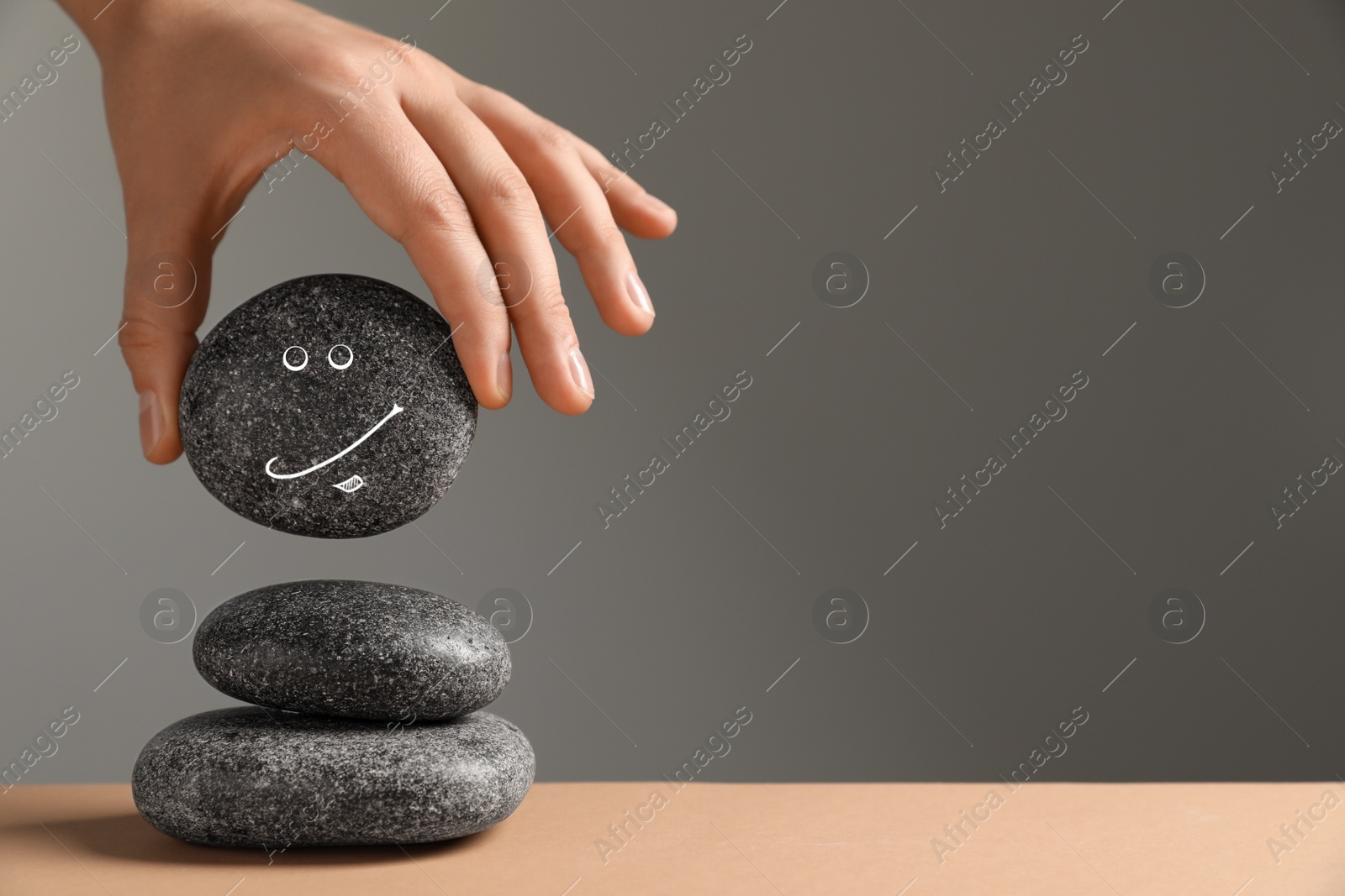Photo of Closeup view of woman putting stone with drawn happy face on stack against grey background, space for text. Zen concept