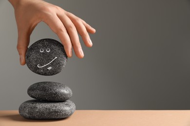 Closeup view of woman putting stone with drawn happy face on stack against grey background, space for text. Zen concept