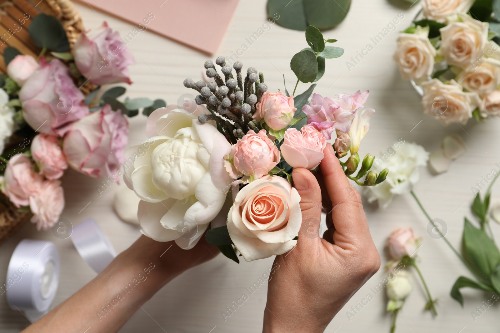 Photo of Florist creating beautiful bouquet at white table, top view