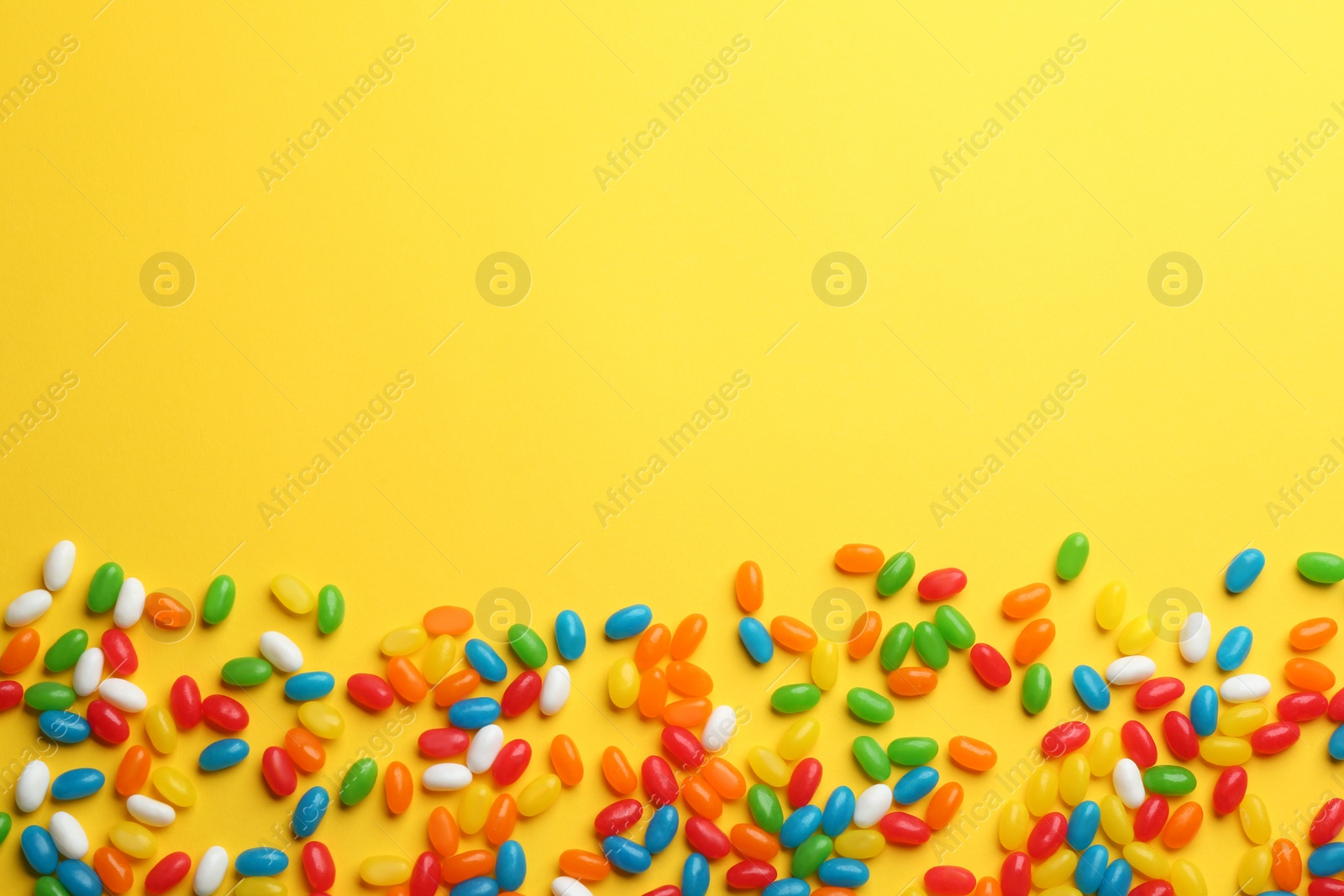 Photo of Tasty colorful jelly beans on yellow background, flat lay. Space for text