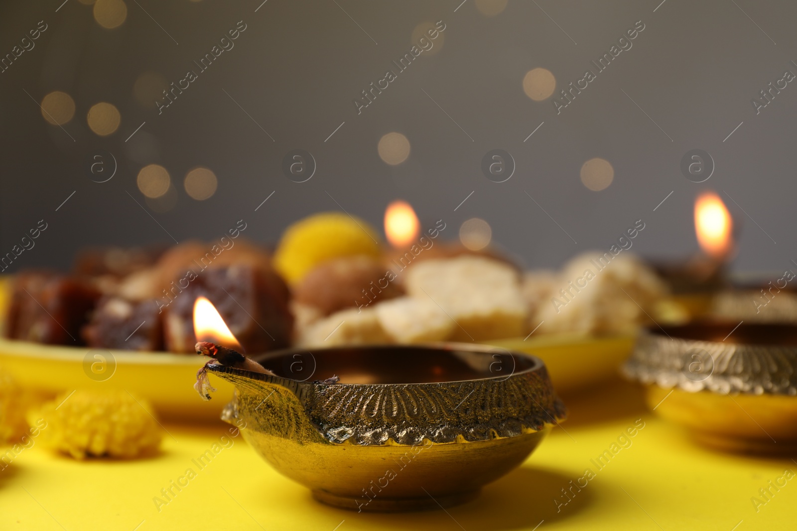 Photo of Happy Diwali. Diya lamp on yellow table against blurred lights, closeup