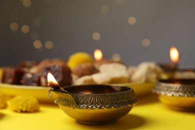 Photo of Happy Diwali. Diya lamp on yellow table against blurred lights, closeup