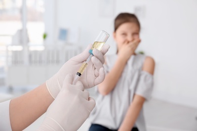 Doctor filling syringe with medicine and child on background. Vaccination day