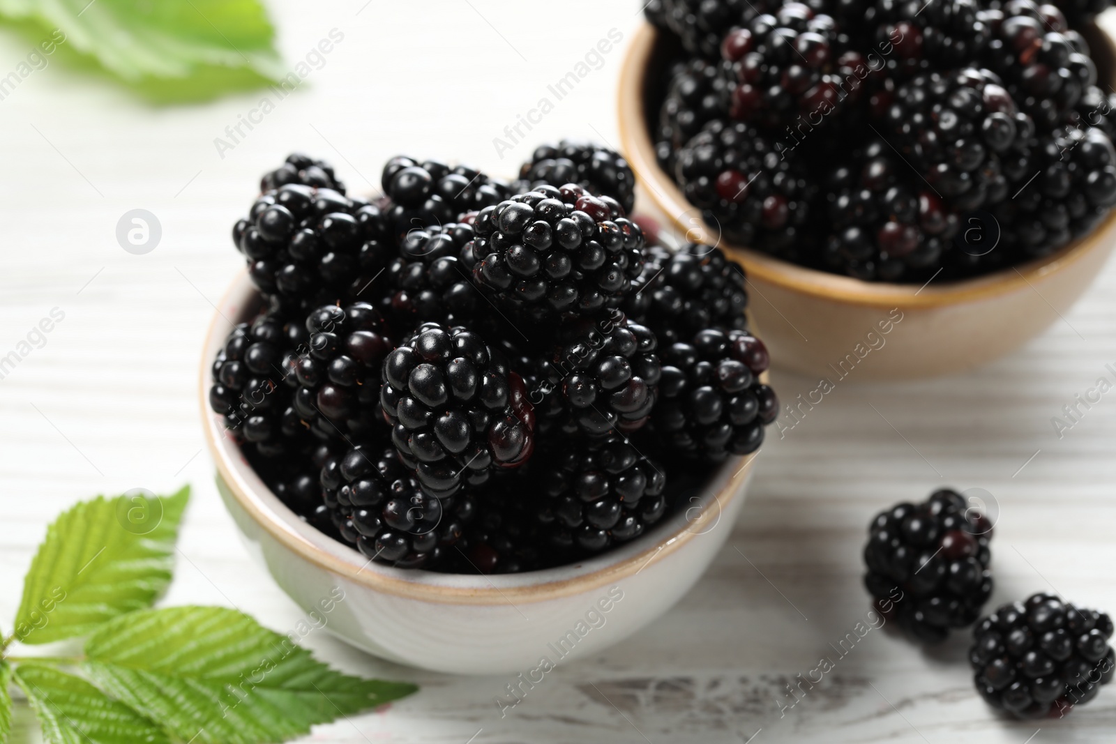 Photo of Ripe blackberries and green leaves on white wooden table, closeup