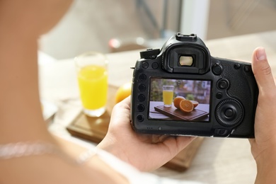 Female photographer taking picture of juice and oranges with professional camera, closeup