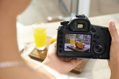 Photo of Female photographer taking picture of juice and oranges with professional camera, closeup