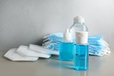 Hand sanitizers and respiratory masks on table against grey background. Protective essentials during COVID-19 pandemic