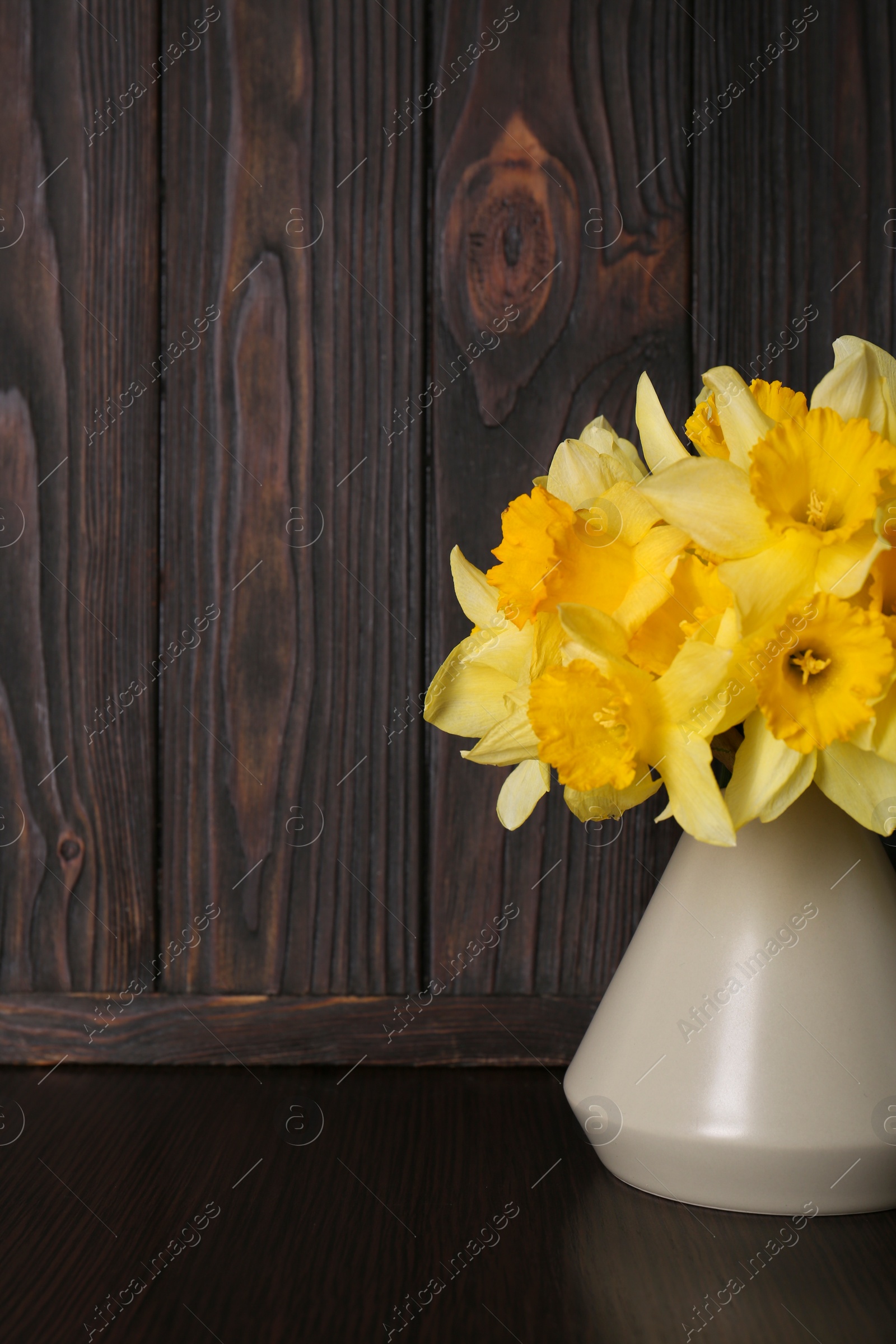 Photo of Bouquet of beautiful yellow daffodils in vase on wooden table. Space for text