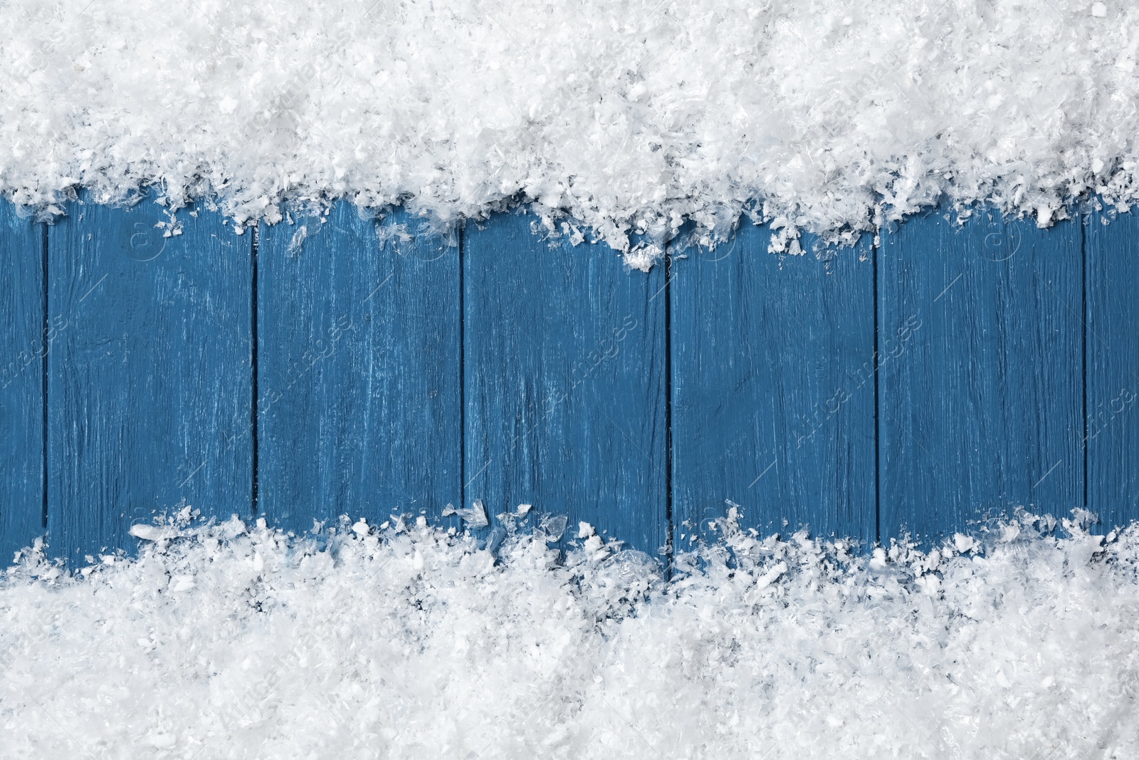 Photo of Frame made of snow on blue wooden background, top view with space for text. Christmas time