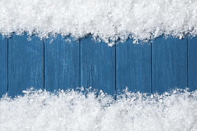 Frame made of snow on blue wooden background, top view with space for text. Christmas time